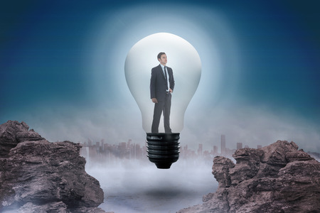 Thinking businessman in light bulb against rocky landscapeの写真素材