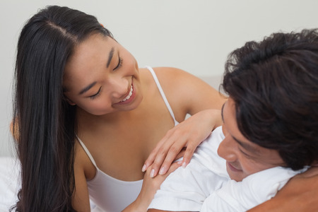 Happy couple lying on bed together at home in bedroomの写真素材