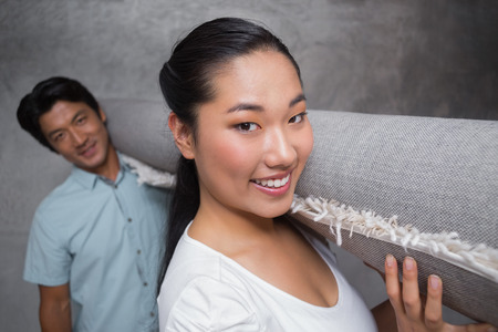 Happy couple holding a rolled up rug in their new homeの写真素材