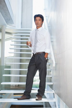 Serious man looking at camera holding champagne flute on the stairsの写真素材