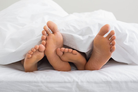 Couples feet sticking out from under duvet at home in bedroomの写真素材