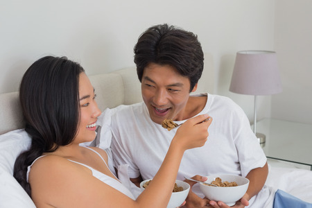 Happy couple having breakfast in bed at home in bedroomの写真素材