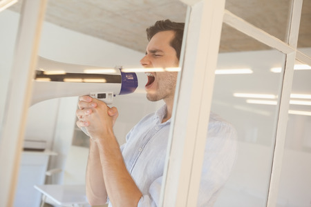 Casual businessman shouting through megaphone in his officeの写真素材