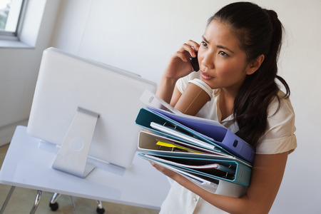 Casual businesswoman balancing coffee on pile of folders in her officeの写真素材