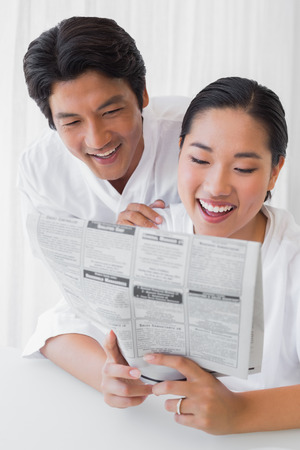 Couple in bathrobes reading newspaper together in the morning at home in the living roomの写真素材