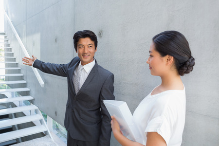 Estate agent showing stairs to customer and smiling outside a houseの写真素材
