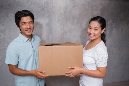Happy couple holding a cardboard moving box in their new homeの写真素材
