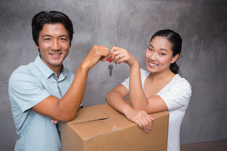 Happy couple holding house key and leaning on moving box in their new homeの写真素材