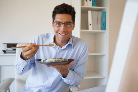 Casual businessman enjoying sushi at his desk in his officeの写真素材