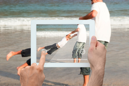 Hand holding tablet pc showing father and son having fun at the beachの写真素材