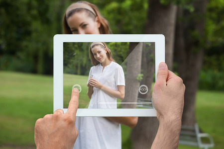 Hand holding tablet pc showing pretty brunette standing in the parkの写真素材
