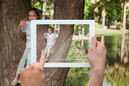 Hand holding tablet pc showing little girl sitting in a tree wavingの写真素材