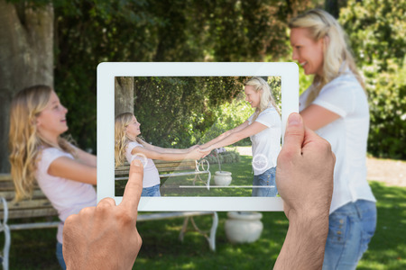 Hand holding tablet pc showing blonde mother and daughter in parkの写真素材