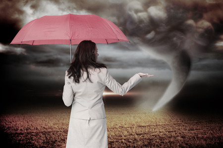 Businesswoman holding umbrella against stormy sky with tornado over fieldの写真素材