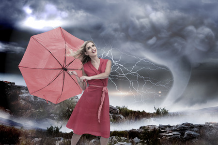 Elegant blonde holding umbrella against stormy sky with tornado over landscapeの写真素材