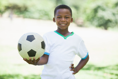 Little boy holding football in the park smiling at camera on a sunny dayの写真素材