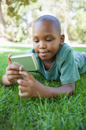Little boy lying on grass looking at digital camera on a sunny dayの写真素材