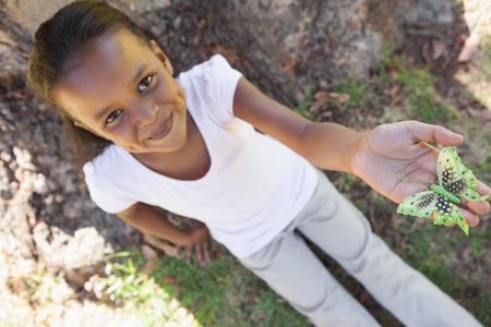 Little girl holding a butterfly in the park smiling at camera on a sunny dayの写真素材