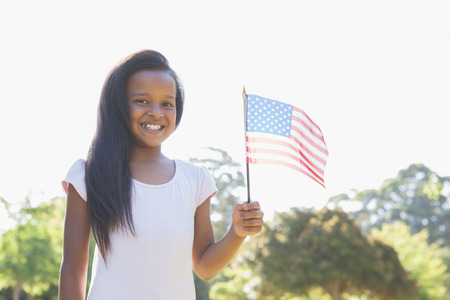 Little girl smiling at camera waving american flag on a sunny dayの写真素材