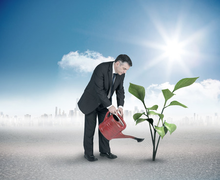 Mature businessman using watering can against cityscape on the horizonの写真素材