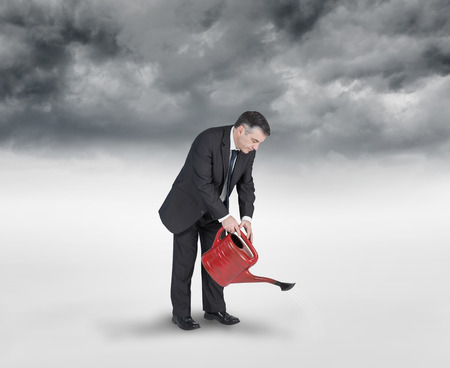 Mature businessman using watering can against stormy sky backgroundの写真素材