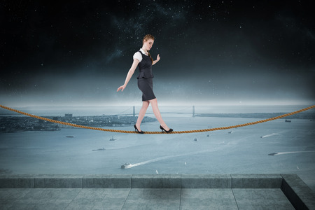 Businesswoman doing a balancing act against balcony overlooking coastline at nightの写真素材