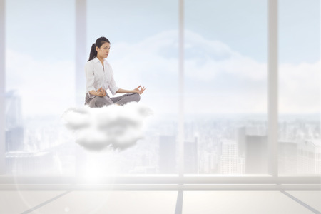 Businesswoman sitting in lotus pose against bright white room with windowsの写真素材