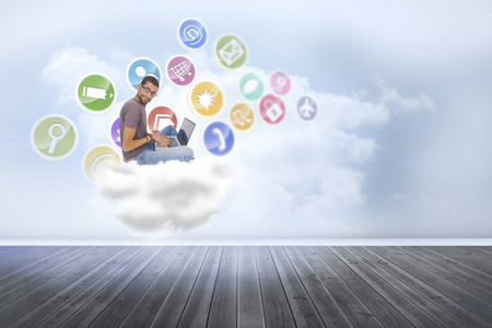 Man wearing glasses sitting on floor using laptop and looking at camera against clouds in a roomの写真素材