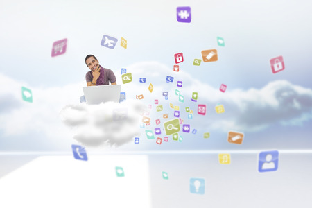 Thinking man sitting on floor using laptop and smiling against clouds in a roomの写真素材