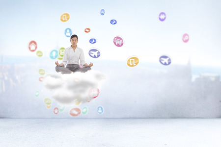 Businesswoman sitting in lotus pose against city scene in a roomの写真素材