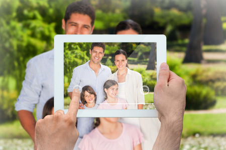 Hand holding tablet pc showing family smiling at camera in parkの写真素材