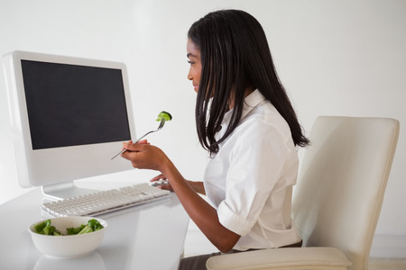 Casual pretty businesswoman eating a salad at her desk in her officeの写真素材