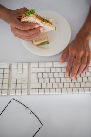 Businesswoman eating a sandwich at her desk in her officeの写真素材