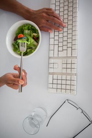 Businesswoman eating a salad at her desk in her officeの写真素材