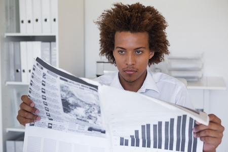 Casual focused businessman reading newspaper at desk in his officeの写真素材