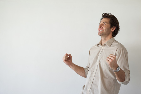 Casual smiling businessman cheering with fists clenched in his officeの写真素材