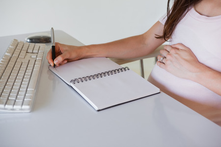 Casual pregnant businesswoman writing at her desk in her officeの写真素材