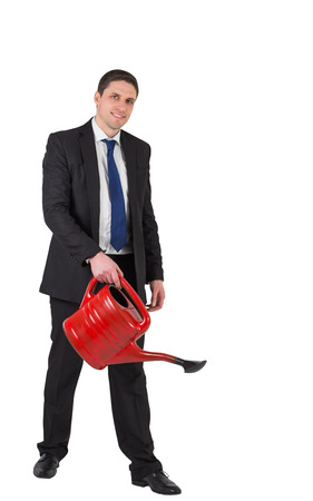 Businessman watering with red can and smiling at camera on white backgroundの写真素材