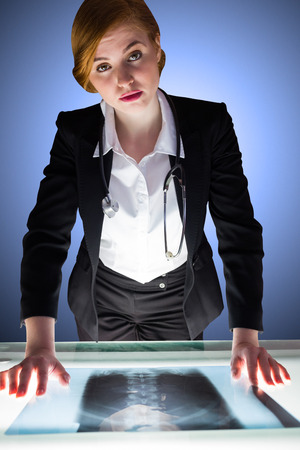 Redhead doctor looking at camera with xray on desk on shadow backgroundの写真素材