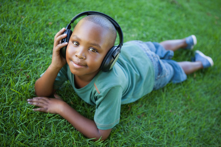 Little boy lying on grass listening to music smiling at camera on a sunny dayの写真素材