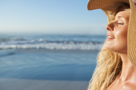 Gorgeous blonde in straw hat smiling on beach on a sunny dayの写真素材