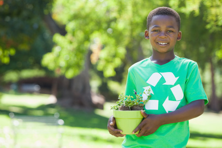 Young boy in recycling tshirt holding potted plant on a sunny dayの写真素材