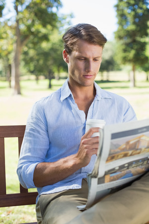 Man sitting on park bench drinking coffee and reading paper on a sunny dayの写真素材