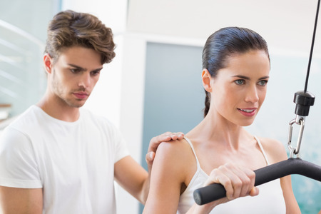 Fit smiling woman using weights machine for arms with her trainer at the gym