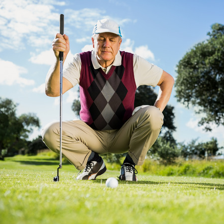 Golfer kneeling watching gold ball on a sunny day at the golf courseの写真素材