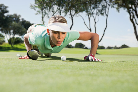 Female golfer blowing her ball on putting green on a sunny day at the golf courseの写真素材