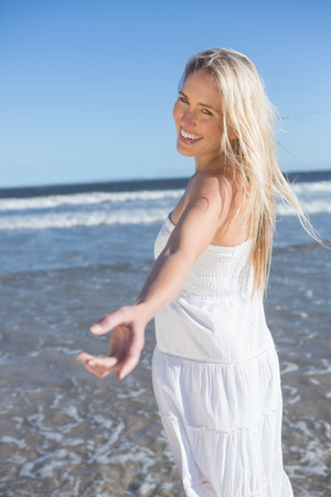 Woman in white dress offering her hand on the beach on a bright dayの写真素材