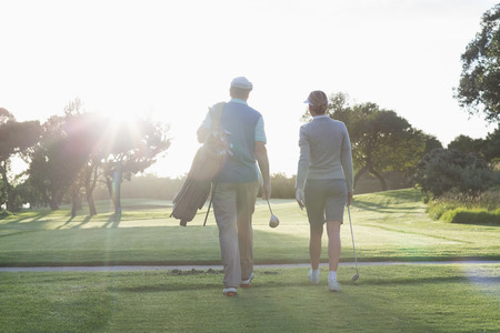 Golfing couple walking and chatting on a sunny day at the golf courseの写真素材