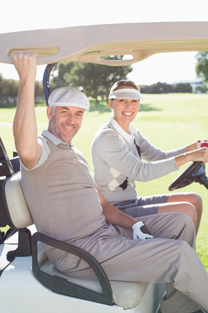 Happy golfing couple smiling at camera in their buggy on a sunny day at the golf courseの写真素材