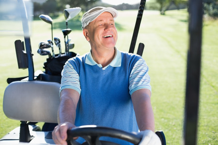 Happy golfer driving his golf buggy on a sunny day at the golf courseの写真素材